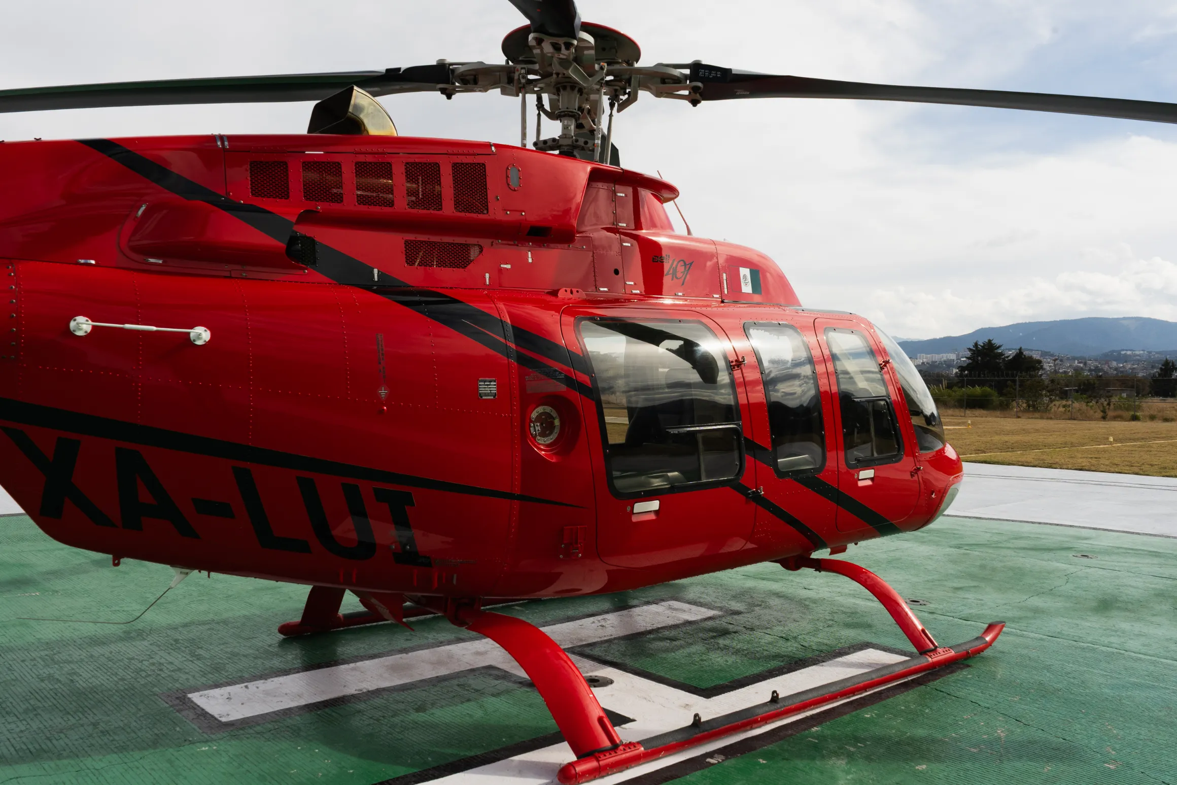 Frente y lateral del helicóptero rojo de 62 Sky Moments en el helipuerto, con la ciudad al horizonte